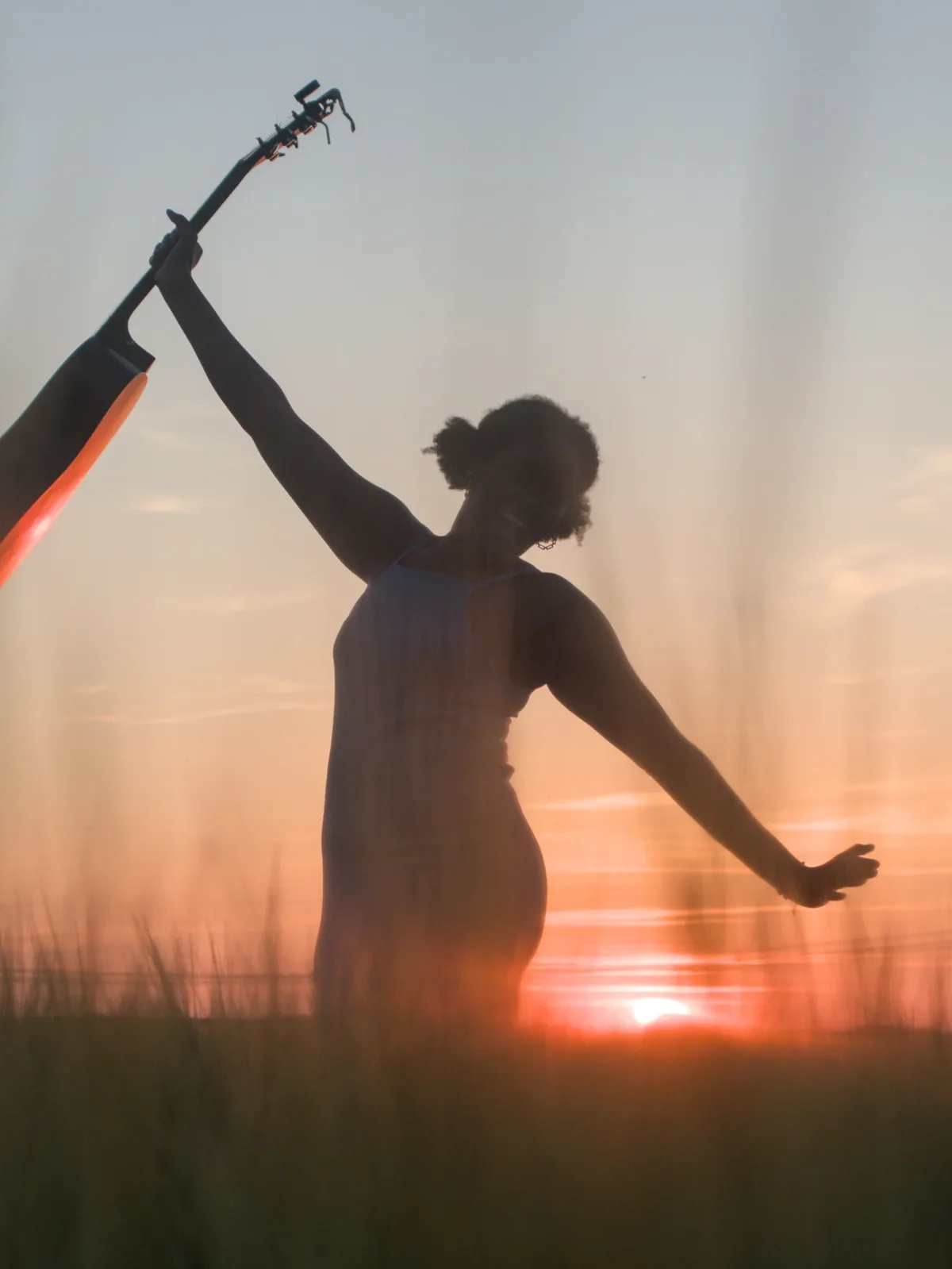 Darlene raising her guitar in a wheat field at sunset
