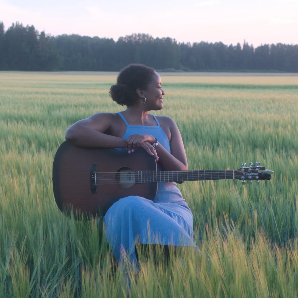 Darlene sitting with her guitar in a wheat field